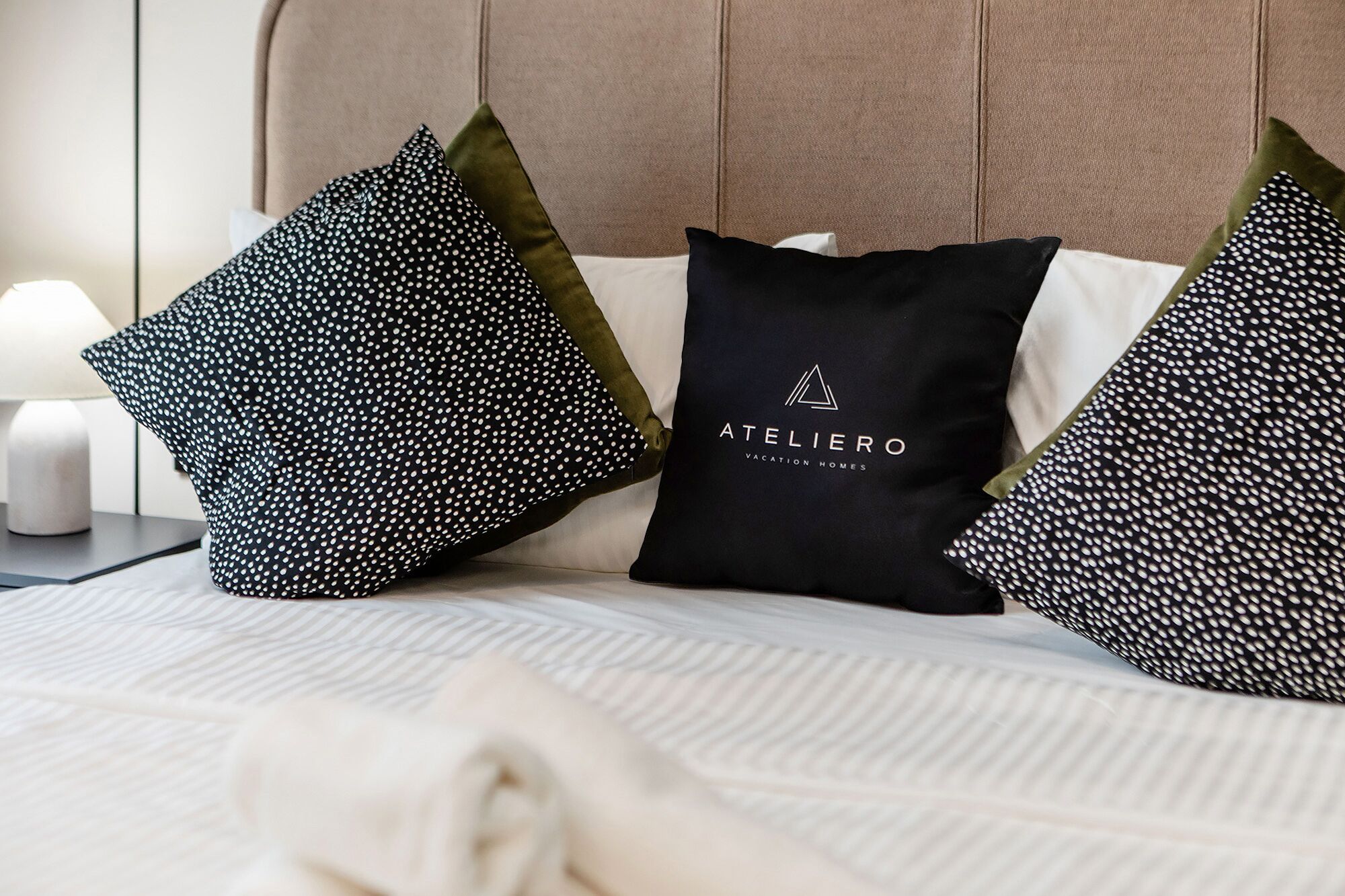 A neatly made bed with a pillow featuring the logo 'ATELIERO VACATION HOMES'.
