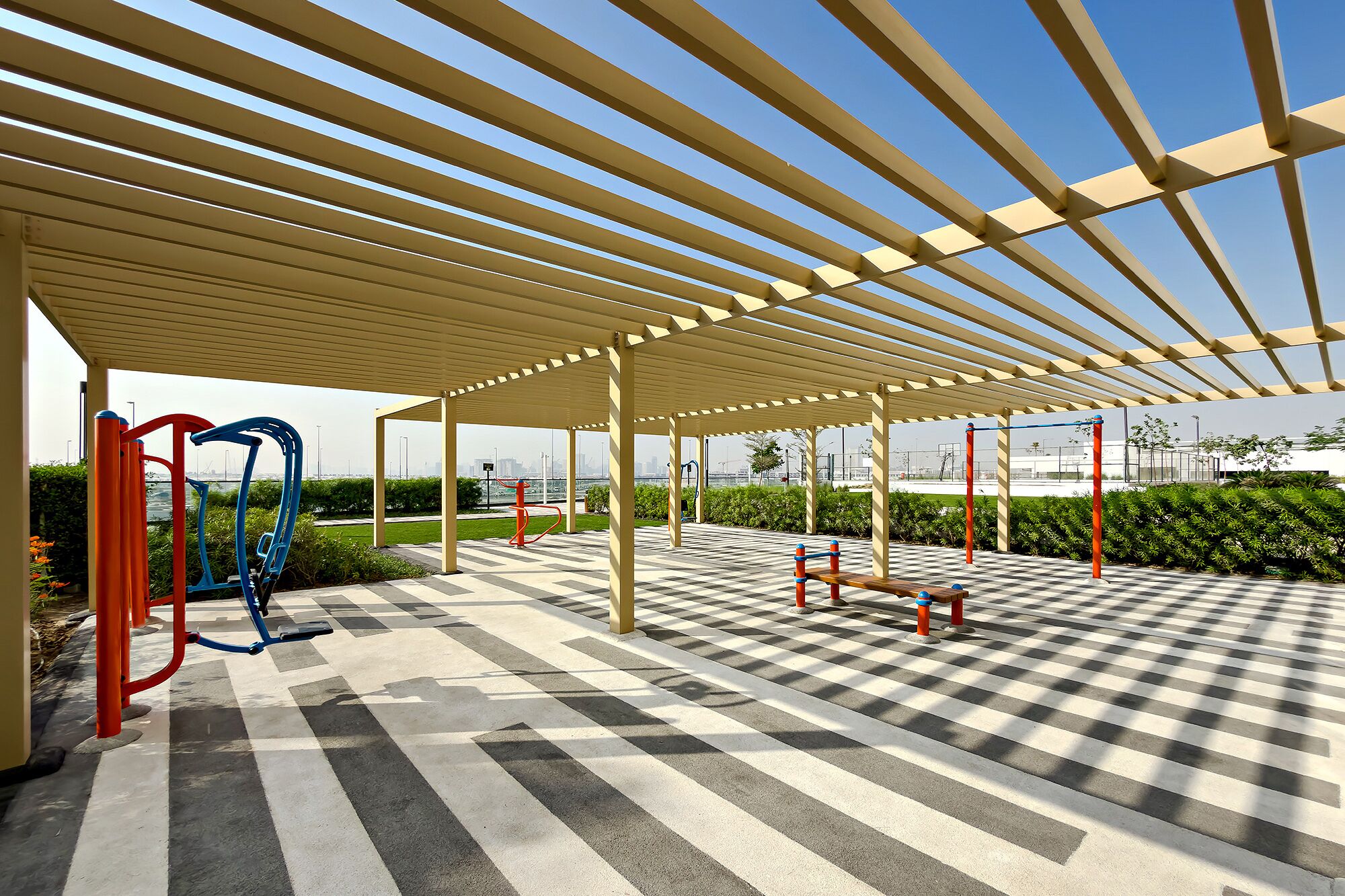 Un área de gimnasio al aire libre con equipo de ejercicio, piso a cuadros y una estructura cubierta con techo.