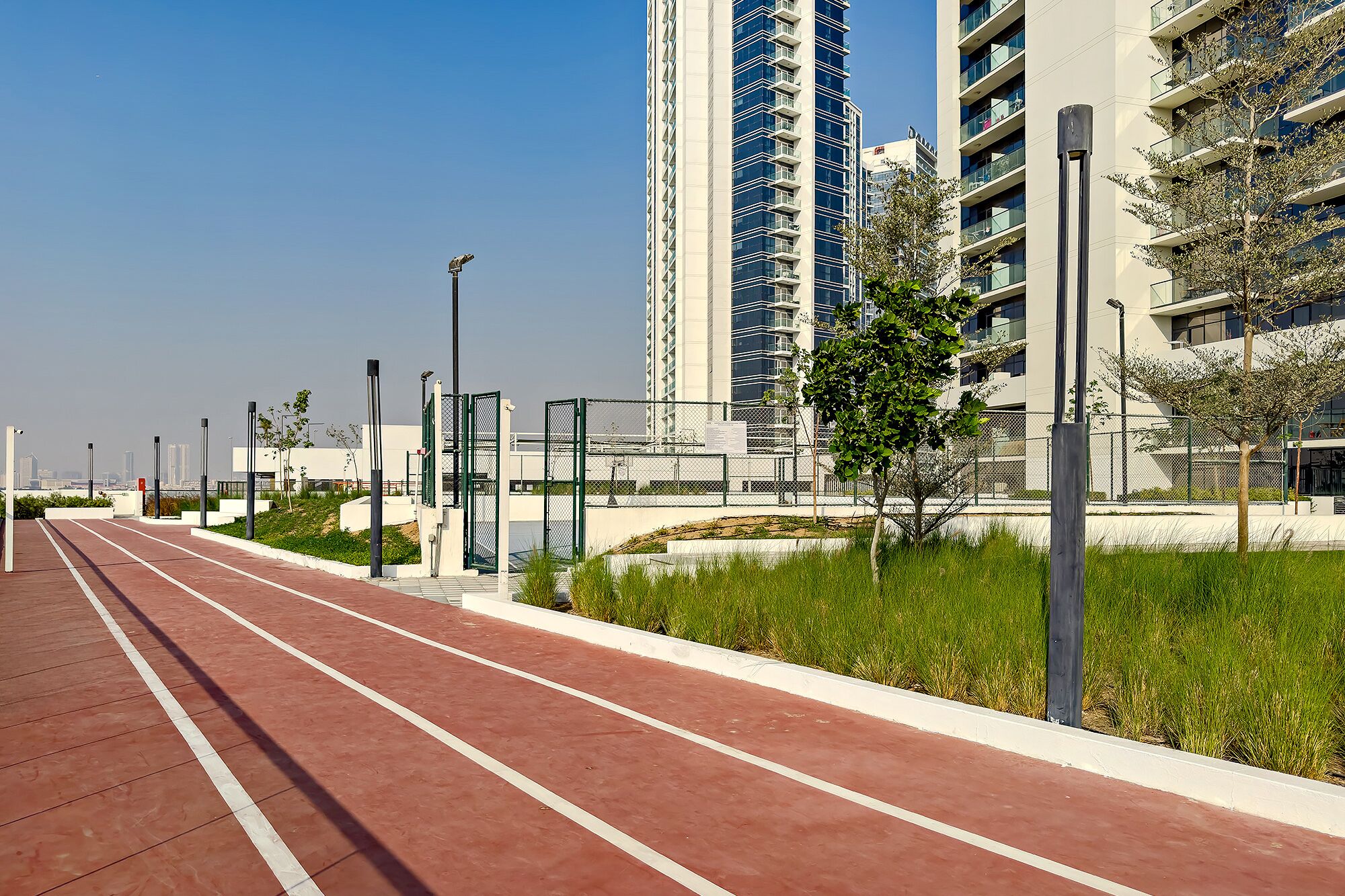 A running track with a red surface, surrounded by greenery and tall buildings.