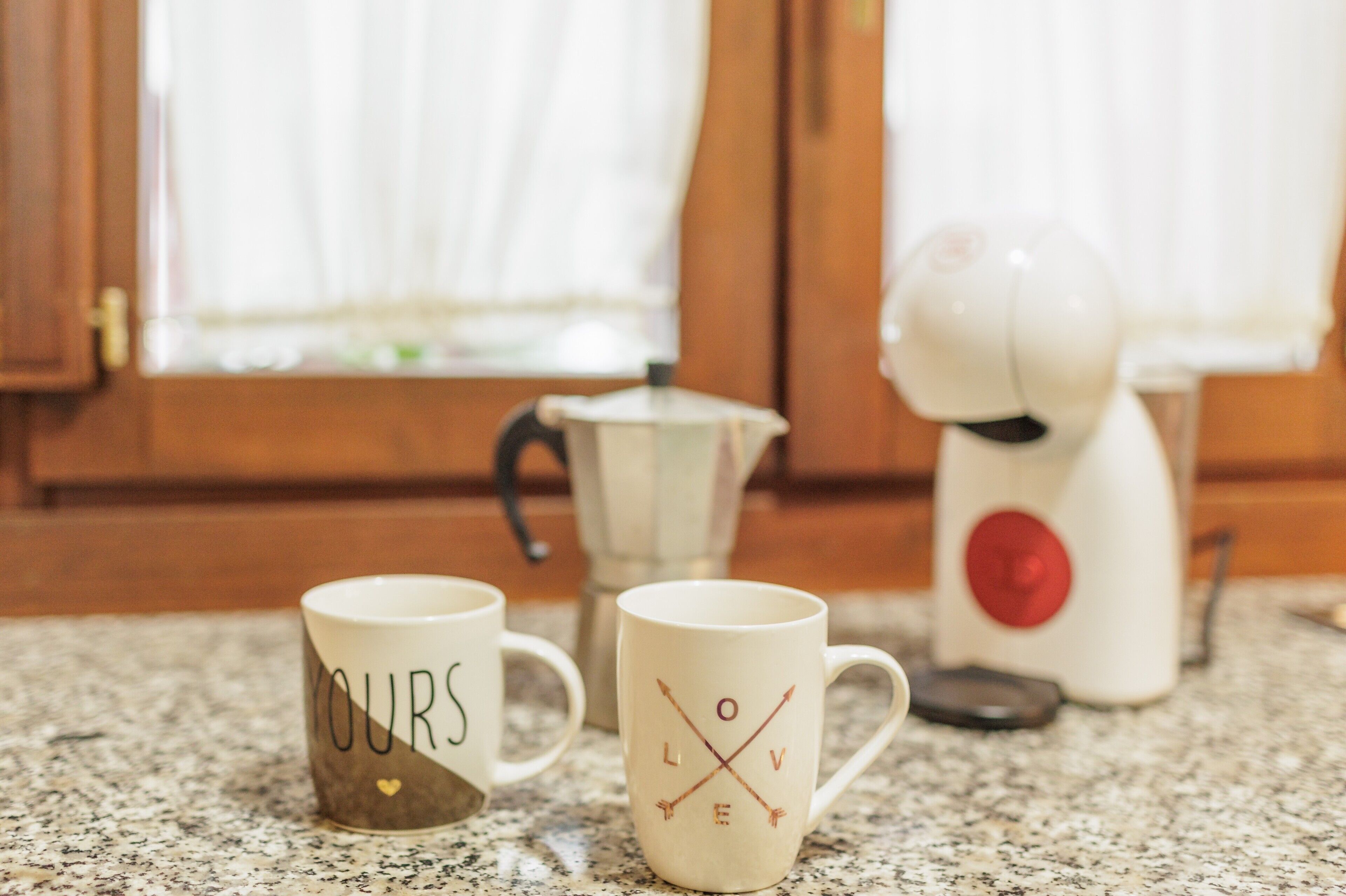 Twee mokken met de tekst 'YOURS' en 'LOVE', een witte theepot en een witte waterkoker op een aanrecht.