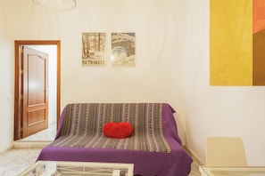 Una habitación con un sofá, una mesa de centro de vidrio y dos cuadros en la pared.