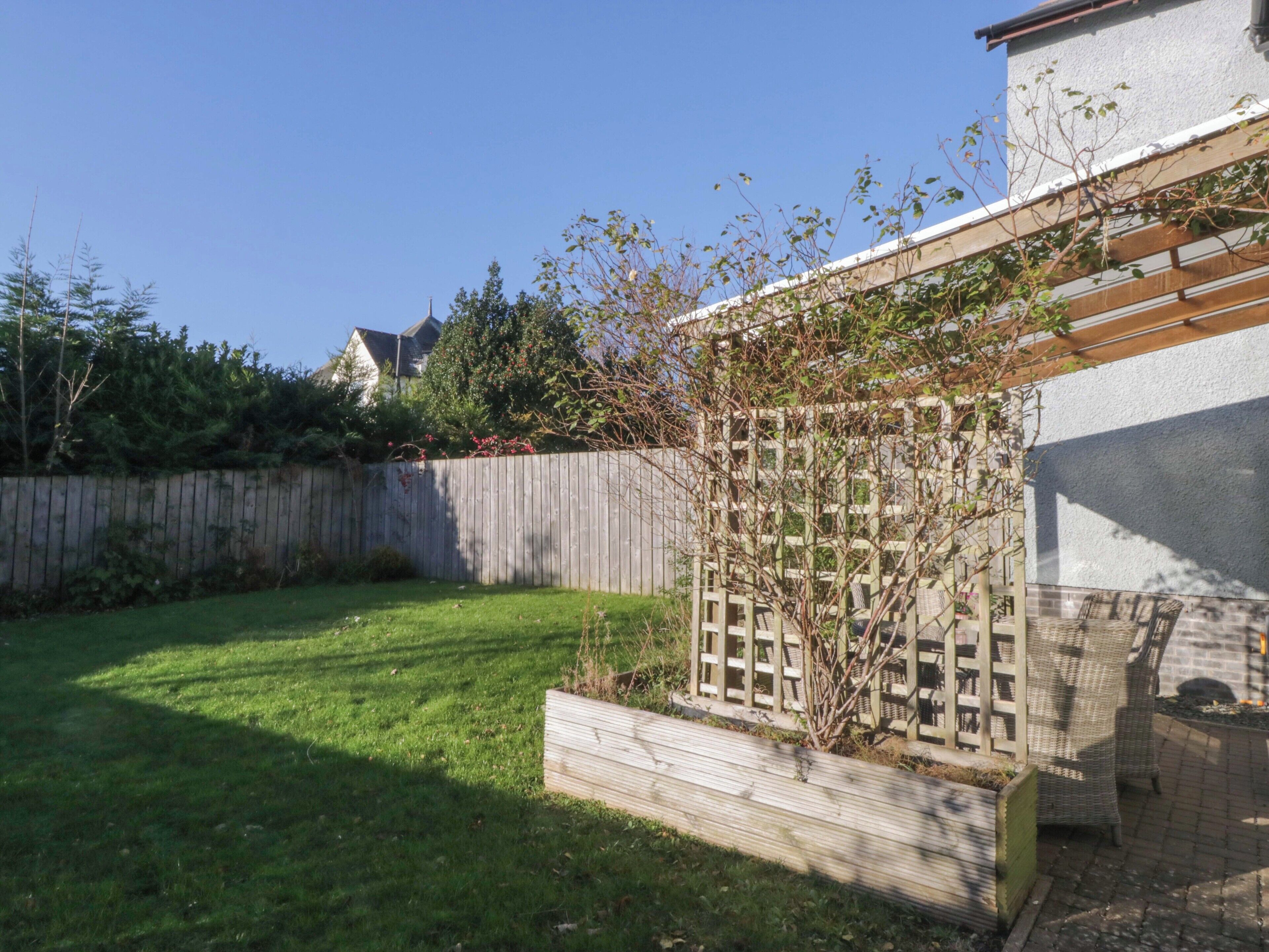 Un jardin avec une clôture en bois, un petit parterre et une pergola agrémentée de meubles en osier.
