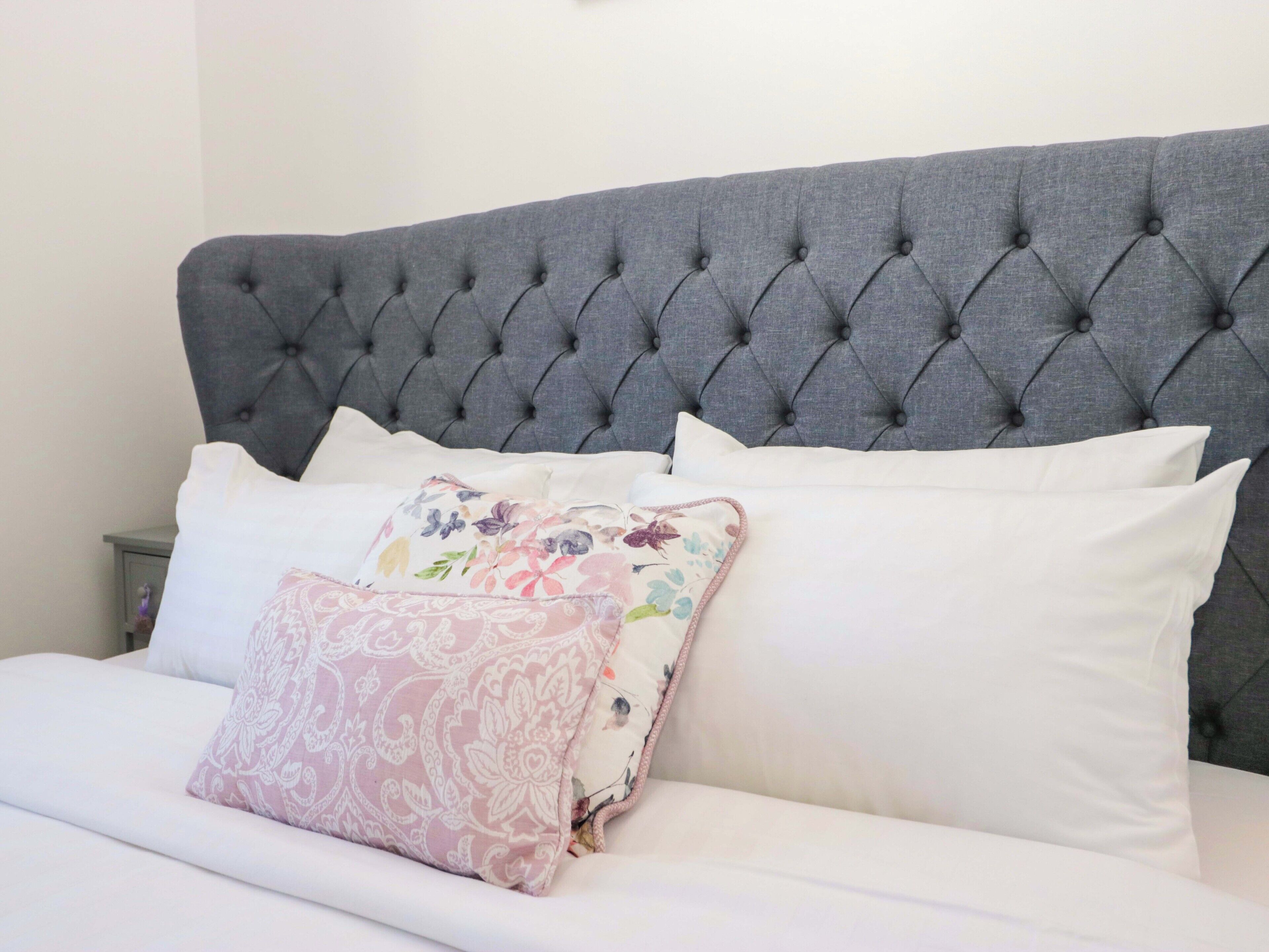 Een bed met een gestoffeerd hoofdeinde, witte beddengoed en decoratieve kussens.