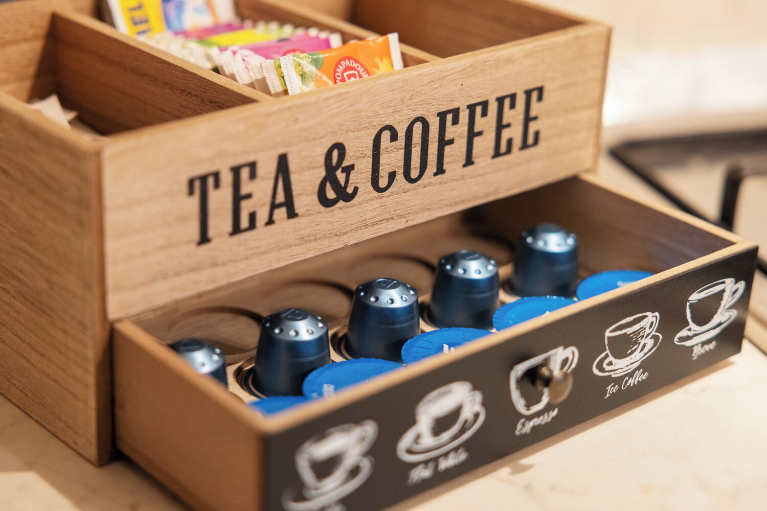 Una caja de madera con la etiqueta 'TÉ Y CAFÉ' que contiene varias cápsulas de café y bolsitas de té.