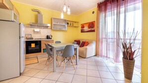 Una cocina compacta con electrodomésticos modernos, un comedor con mesa y sillas, y una sala de estar con sofá y un amplio ventanal con cortinas.