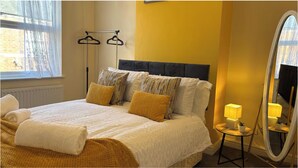 A neatly made bed with a white duvet and two pillows, a bedside table with a lamp, a mirror, and a window with sheer curtains. - Warm and Cosy Two bed Property /Near York City Centre (York)