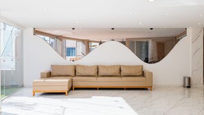 A modern interior with a beige sectional sofa, a glass wall, and a marble floor. - Atrios Beach Hotel (Natal)