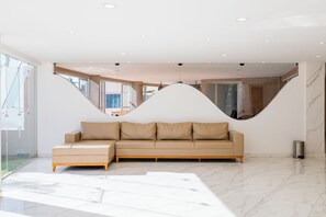 A modern interior with a beige sectional sofa, a glass wall, and a marble floor. - Atrios Beach Hotel (Natal)