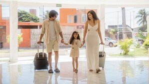 A family with suitcases in a hotel lobby with a glass wall, a sign indicating the exit, and a view of the street outside. - Atrios Beach Hotel (Natal)