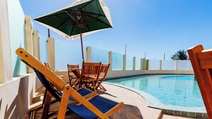A poolside area with wooden lounge chairs and a table, an umbrella, and a clear blue sky. - Atrios Beach Hotel (Natal)