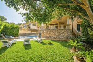A pool area with lounge chairs, a stone wall, and a staircase leading to a balcony.