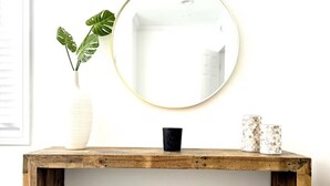 Una consola de madera con un espejo redondo, un taburete pequeño y elementos decorativos.