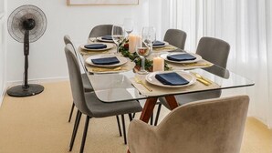Un comedor moderno con una mesa de vidrio, sillas tapizadas en gris y un ventilador de techo.