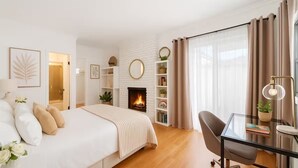 Un dormitorio moderno con cama, escritorio, chimenea y una ventana grande con cortinas.