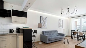 A modern kitchen with a built-in oven, a grey sofa, a dining table with chairs, and a chandelier. - Air-conditioned Apartment | Balcony, Parking and Workspace (Kraków)