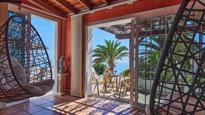 Ein Balkon mit Korbstühlen, einem Tisch mit Getränken und Blick auf Palmen und das Meer.