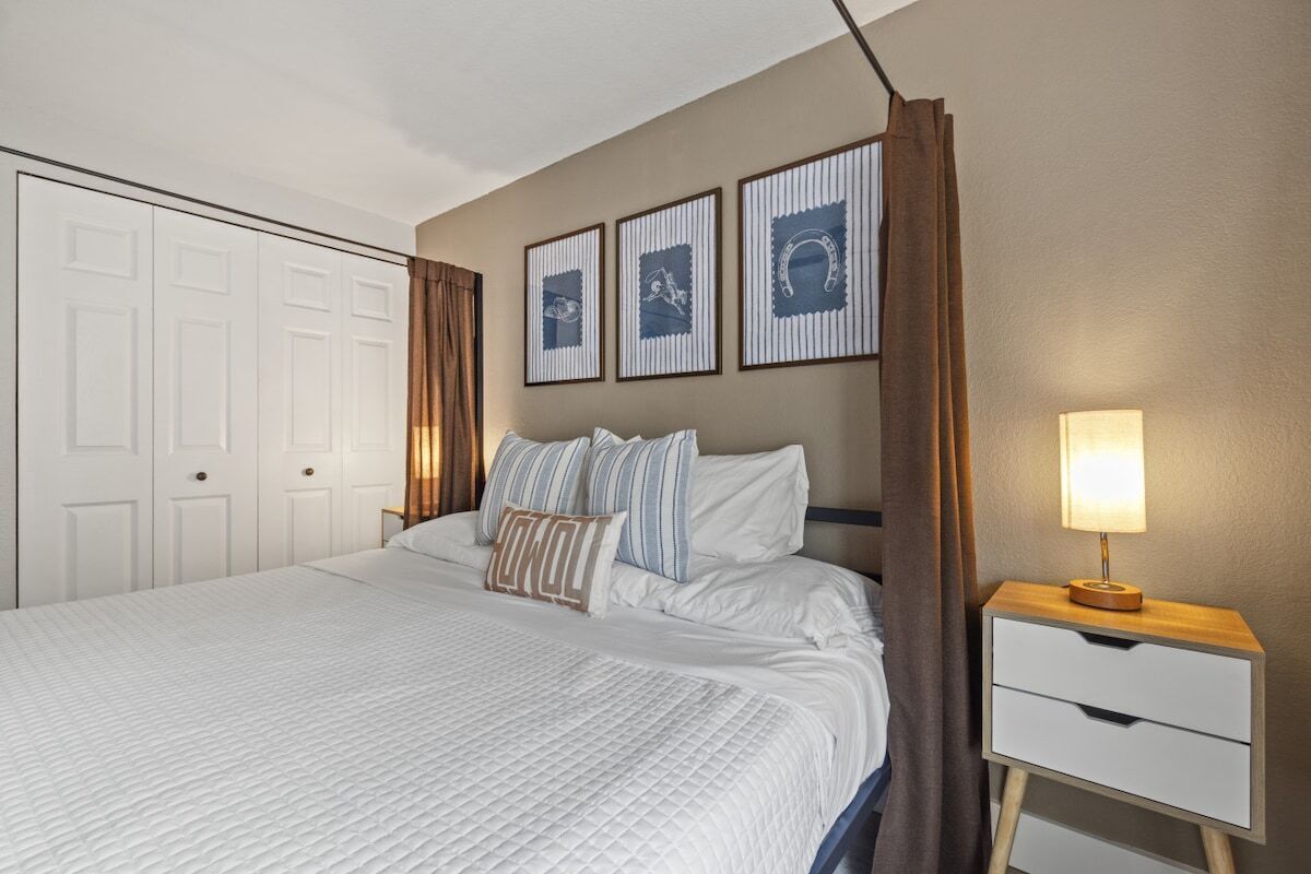 A neatly made bed with a quilted cover, a bedside table with a lamp, and a wall with framed pictures.