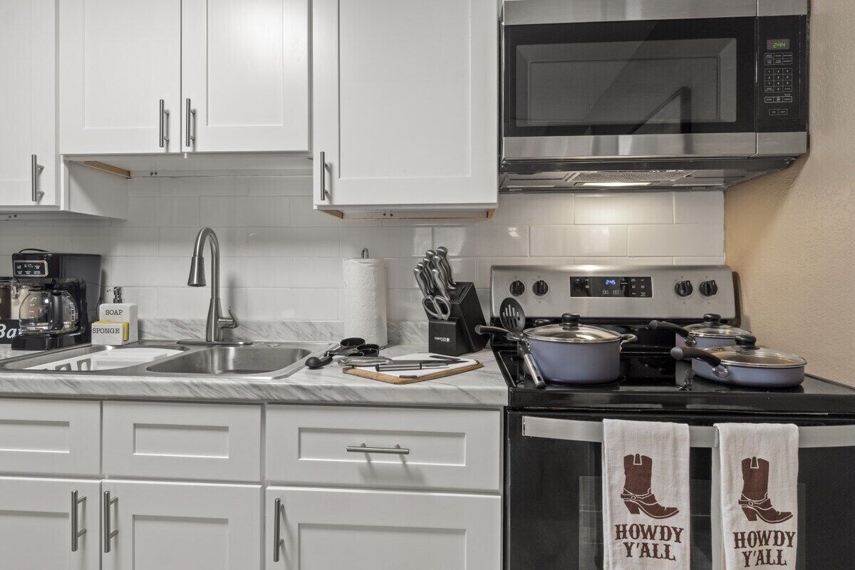 Une cuisine avec des armoires blanches, un four à micro-ondes, une cuisinière et deux serviettes ornées de l’inscription « HOWDY Y’ALL ».