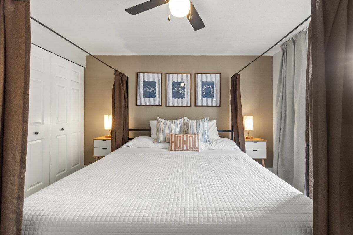 Ein Hotelzimmer mit einem Bett, Nachttischlampen, einem Deckenventilator und gerahmten Kunstwerken an der Wand.