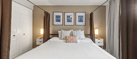 Una habitación de hotel con cama, lámparas de noche, ventilador de techo y cuadros en la pared.