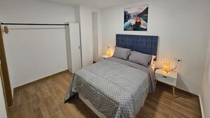Et soveværelse med seng, et natbord, en væglampe, en dør og et maleri.