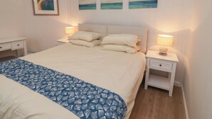 A bedroom with a bed, two bedside tables, a nightstand, and a wall with three paintings. - Braeburn (Bamburgh)