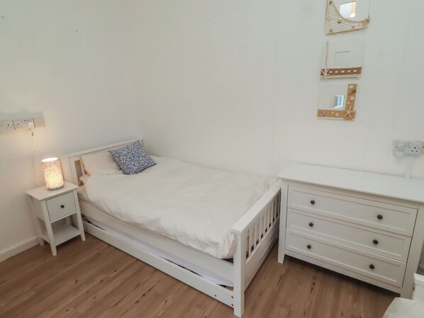 Une chambre avec un lit simple, une table de chevet avec une lampe, une commode et un miroir fixé au mur.
