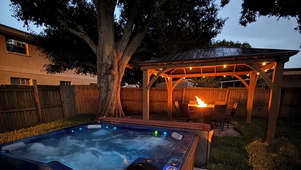 A hot tub in a backyard with a wooden deck, a pergola, and a large tree. - Private Hot Tub - Close to Beaches - Fun Game Room (Clearwater)