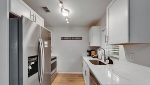 A modern kitchen with a stainless steel refrigerator, a built-in oven, a sink, and a wall-mounted light fixture. - Private Hot Tub - Close to Beaches - Fun Game Room (Clearwater)
