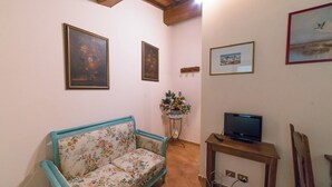 A living room with a floral sofa, a television on a wooden stand, and framed artwork on the walls. - Apartment in the heart of Tuscan nature. Pets allowed (Castelfranco Piandiscó)
