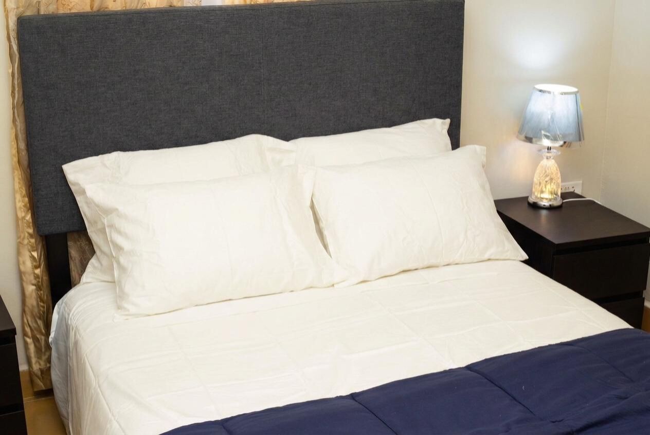 A bed with white bedding and a dark headboard, a bedside lamp, and a dark nightstand.