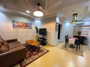 Un salon comprenant un canapé, une table basse, un téléviseur et un coin repas avec une table et des chaises.