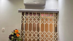 Een kamer met een aan het plafond gemonteerde airconditioner, een schuifdeur met een lattenwerkpatroon, en een bloemstuk op de vloer.
