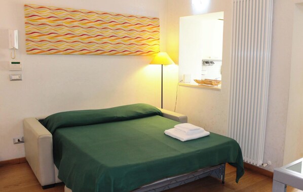 A neatly made bed with a green bedspread, a bedside lamp, and a towel on the bed. - Garden House (Bari)