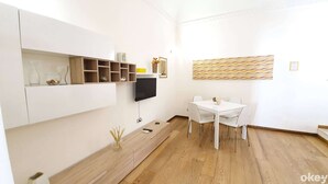 A modern living room with a flat-screen TV, a dining table with chairs, a wooden floor, and a decorative wall piece. - Garden House (Bari)