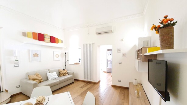 A modern living room with a sofa, a dining table with a plate of pastries, a TV, and a wall-mounted air conditioner. - Garden House (Bari)