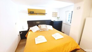 A neatly made bed with a yellow bedspread and white pillows, a black headboard, a small bedside table with a lamp, and a window with a view of the outside. - Garden House (Bari)