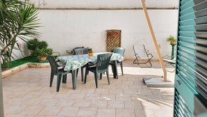 An outdoor patio with a table and chairs, surrounded by potted plants and a decorative wall panel. - Garden House (Bari)