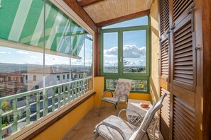 Un balcone con vista sugli edifici, una sedia, un tavolo e una finestra con persiane.