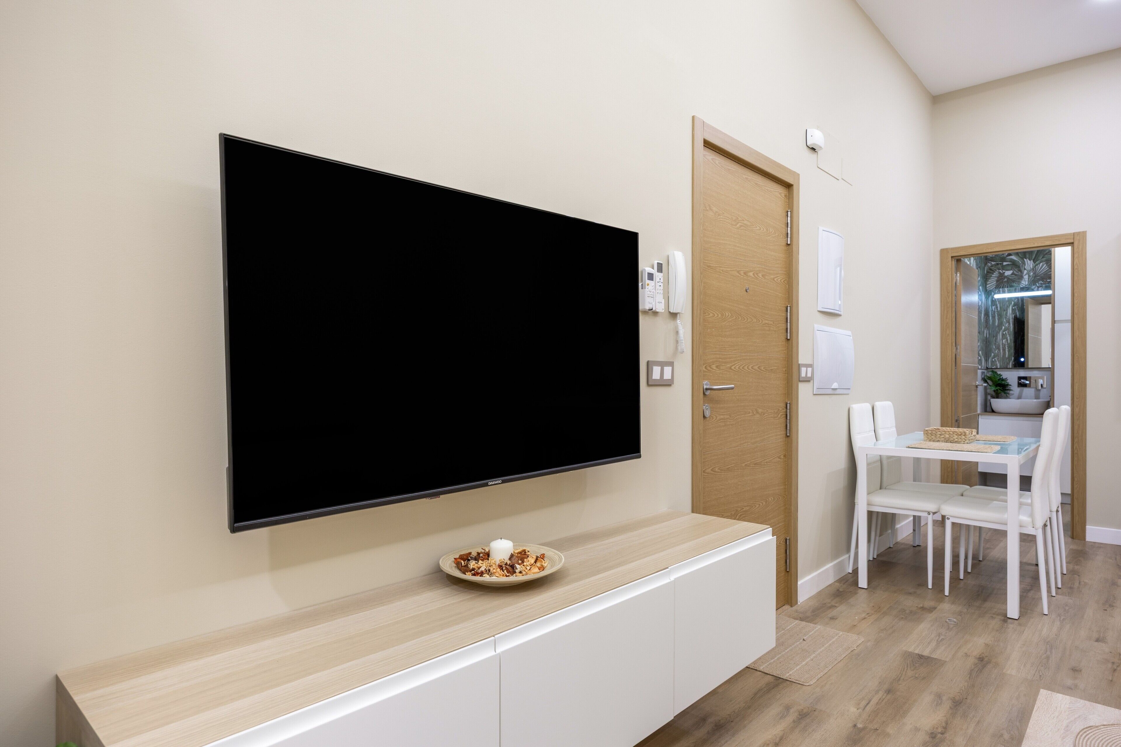 Un salon moderne doté d’un téléviseur à écran plat fixé au mur, d’un coin repas avec une table et des chaises, et d’une porte en bois.
