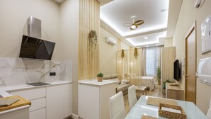 Eine moderne Küche mit Einbauherd, ein Essbereich mit Glastisch und ein Wohnbereich mit Sofa und Fernseher.