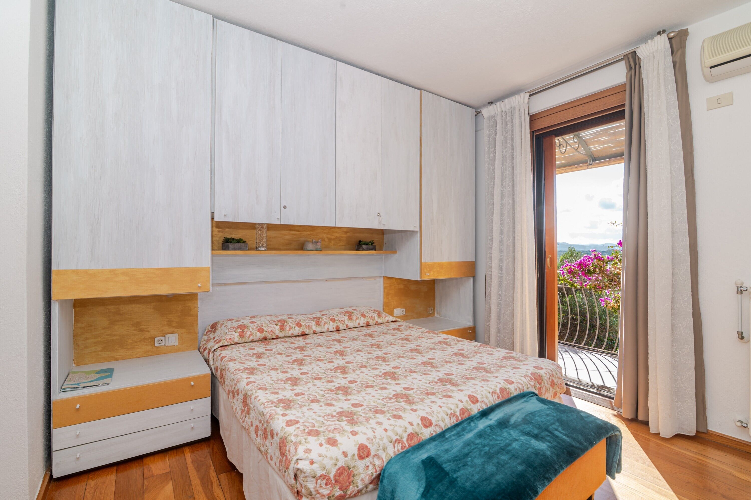 A bedroom with a bed, wooden wardrobe, and a balcony with a view.