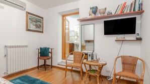 A room with a bed, two wicker chairs, a small table, a TV, a bookshelf, and a radiator. - Room 'La Chicca Di Francesca- Room 3' with Private Terrace, Wi-Fi and Air Conditioning (Santa Teresa Gallura)