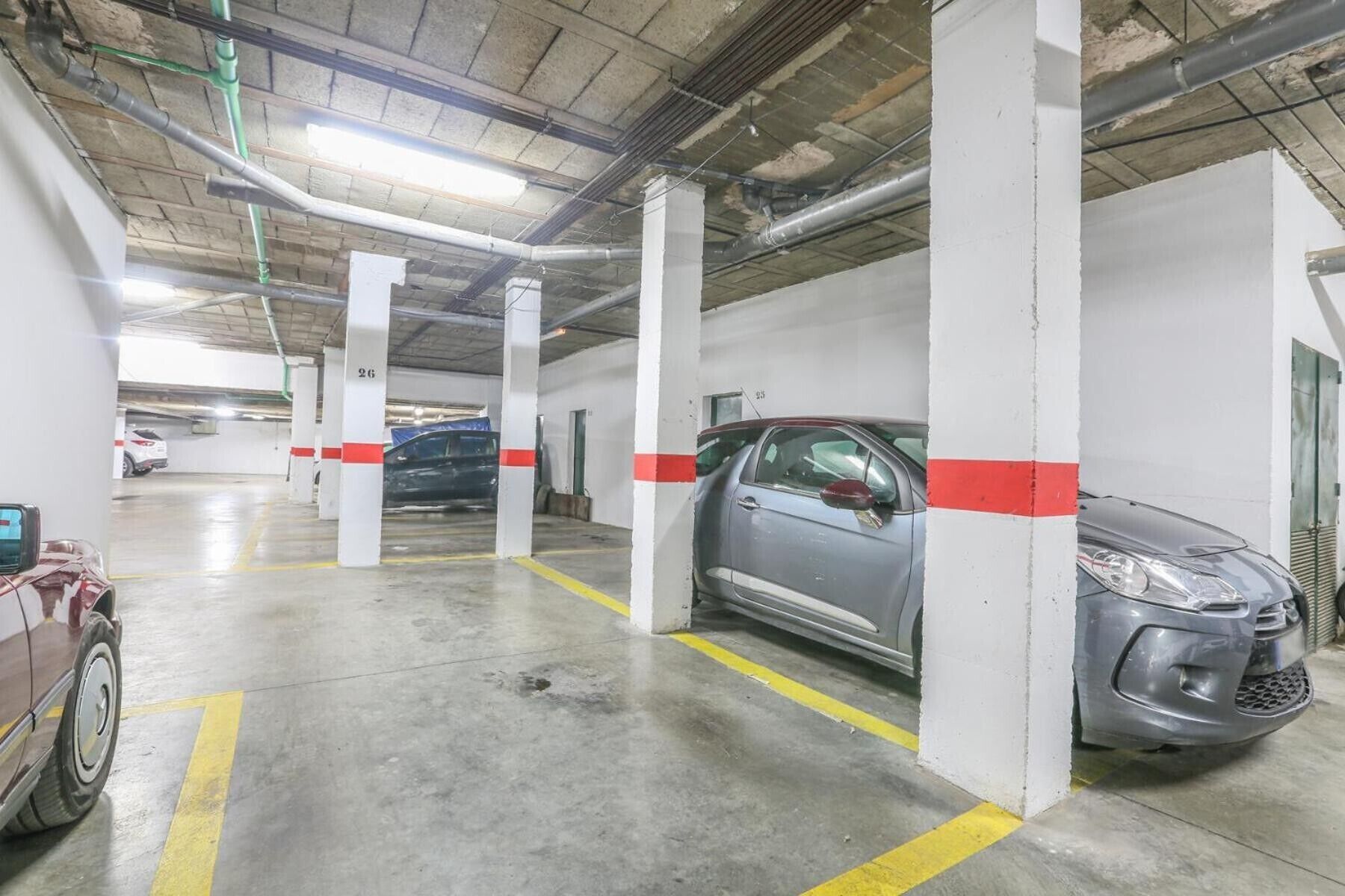 En parkeringskælder med flere niveauer, støttepiller i beton, gule parkeringsmarkeringer og biler parkeret på anviste pladser.