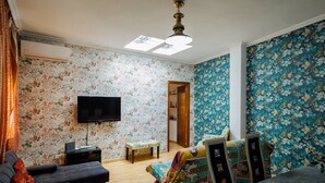 A room with a sofa, a TV, a small table, a colorful chair, and a ceiling fan. - 'Juderia Center Premium Suites Free Parking' Apartment with Balcony, Wi-Fi & Air Conditioning (Seville)