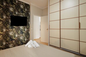 A hotel room with a bed, a wall-mounted TV, a sliding door, and a door leading to another room.