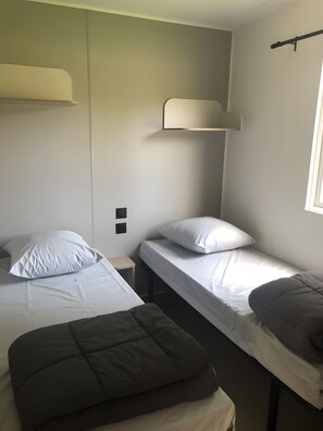 A small, single-room accommodation with two single beds, a bench, and a window. - “Riviera 47” Mobile Home with Shared Pool, Communal Terrace, and Wi-Fi (Saint-Gervais)