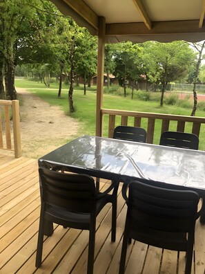 A covered outdoor area with a table and chairs, surrounded by trees and a grassy path. - “Riviera 47” Mobile Home with Shared Pool, Communal Terrace, and Wi-Fi (Saint-Gervais)