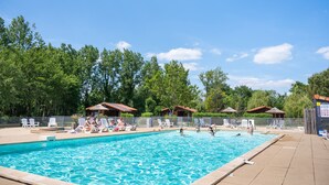 Una piscina con sillas de descanso y sombrillas, rodeada de árboles y edificios pequeños.
