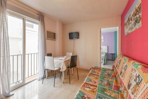 A living room with a sofa, a dining table with chairs, a TV mounted on the wall, and a balcony with a curtain. - Duque Center Premium Suites Apartment with Balcony, Wi-Fi & Air Conditioning (Seville)